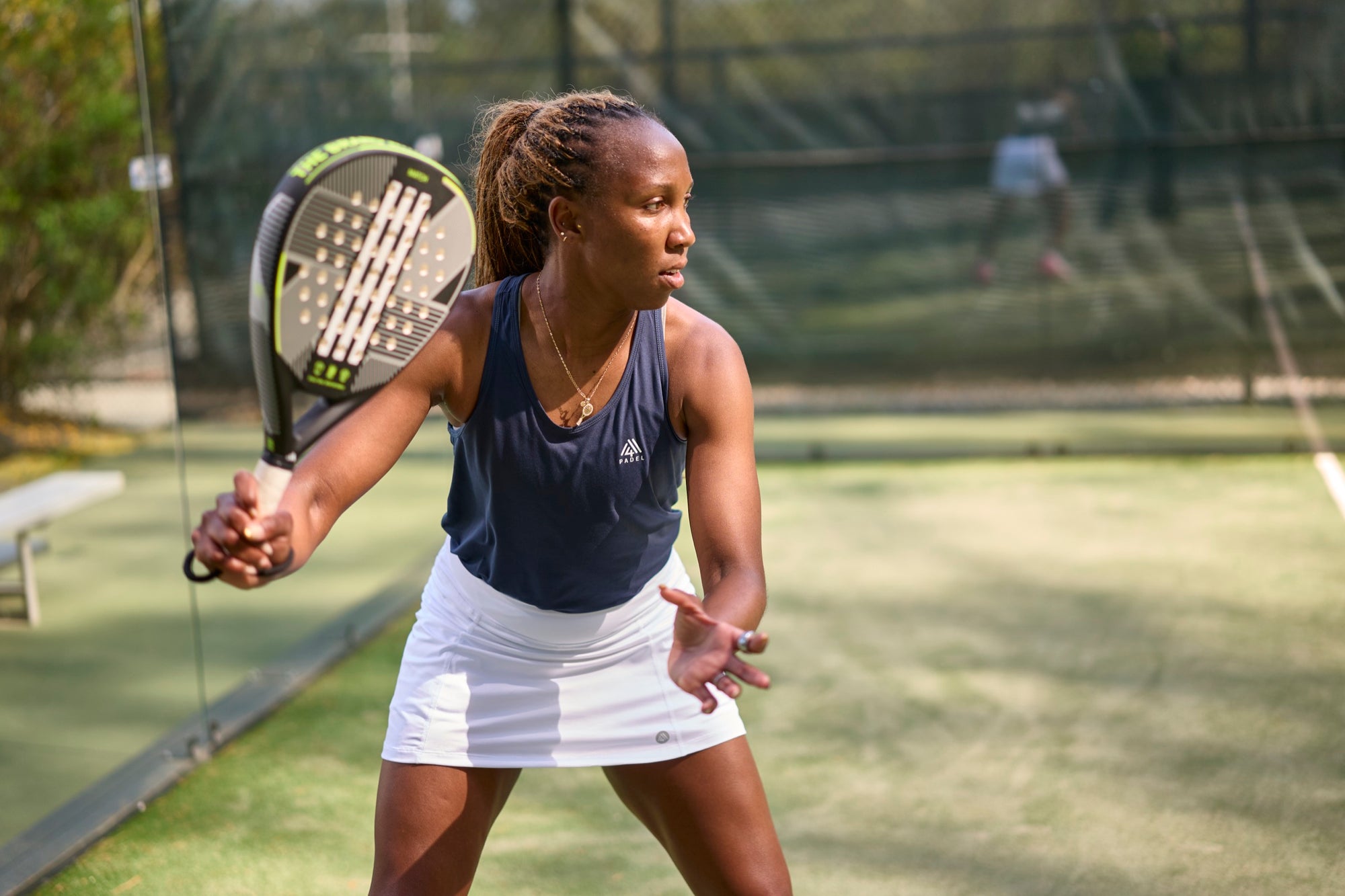 Woman in M4 padel kit ready at the net on a sunlit summer court